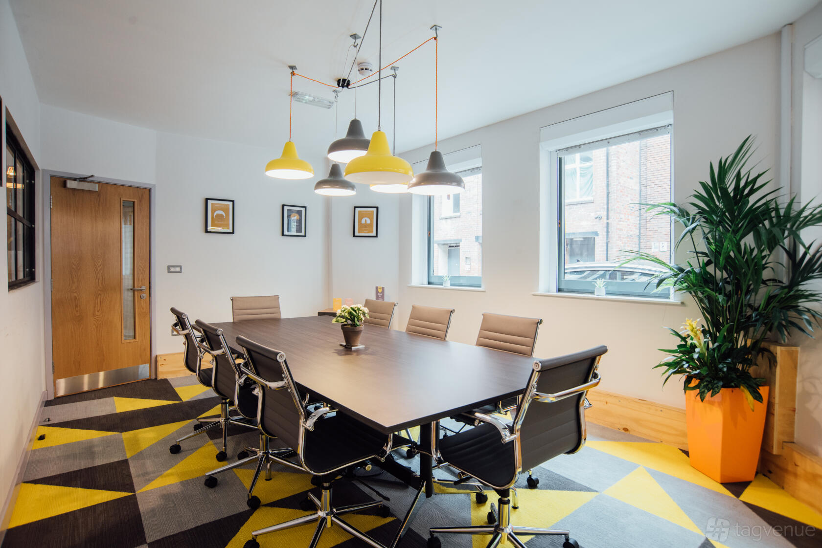 A meeting room with a large conference table, swivel chairs, geometric rug, and pendant lighting at Wizu Workspace - Leeds - Number 32.