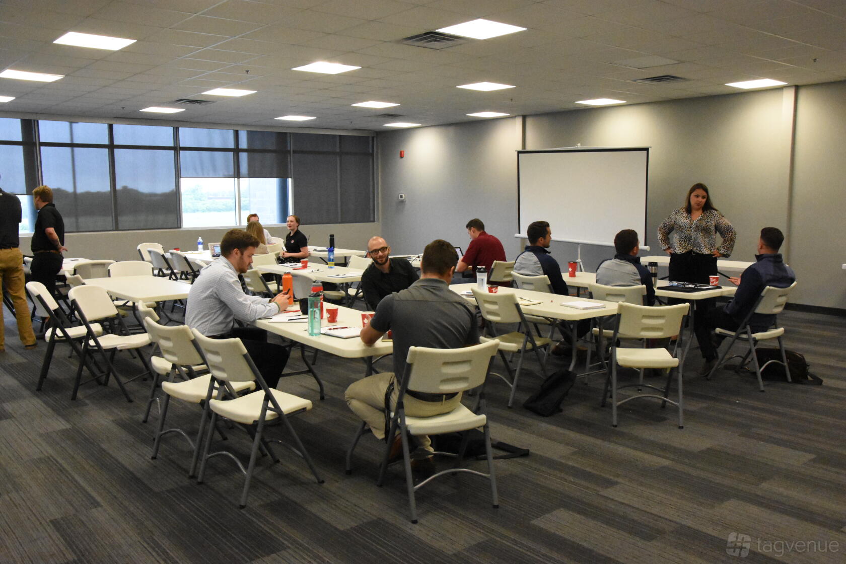 A meeting room with folding tables, white plastic chairs, gray carpeting, and a projector screen at Toronto Rock Athletic Centre.
