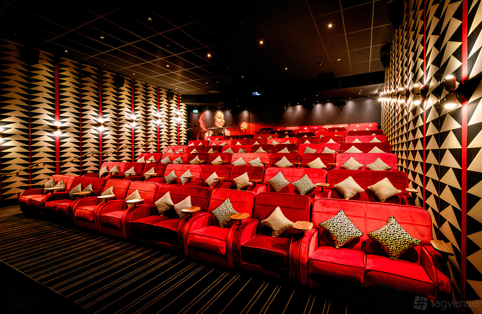 A screening room with tiered rows of red velvet armchairs, patterned walls, and accent pillows at Everyman Borough Yards.