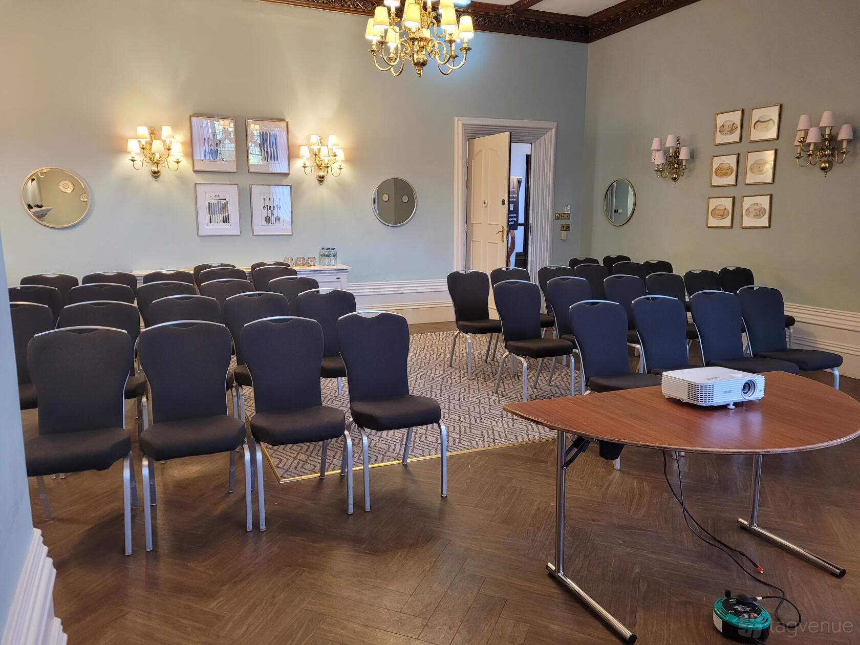 A meeting room with rows of black chairs, wall sconces, framed art, and a projector at Mercure Sheffield Kenwood Hall Hotel & Spa.