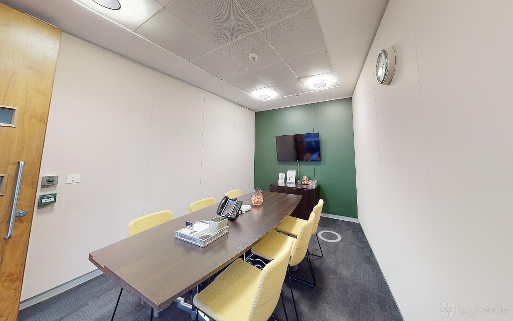 A meeting room with a long wooden table, yellow chairs, wall-mounted screen, and green accent wall at Landmark: Chancery Place, Manchester.