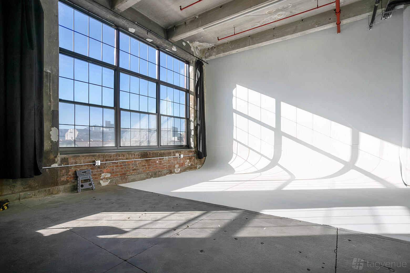 A photo studio with a white cyclorama wall, concrete floors, and large industrial windows at MikSpace - Stewart Ave.