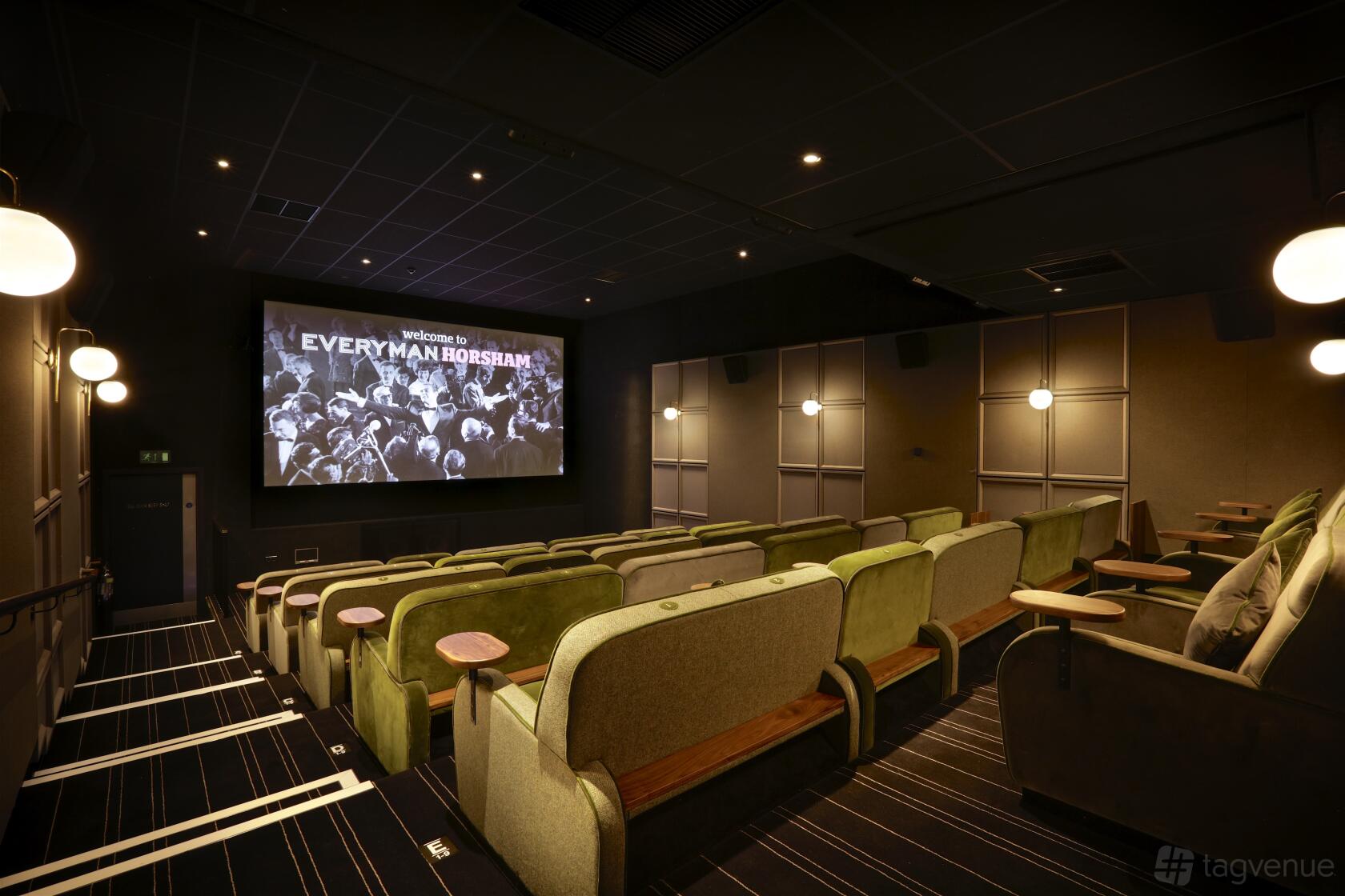 An auditorium with tiered velvet seating, wall sconces, and a large projection screen at Everyman Horsham.