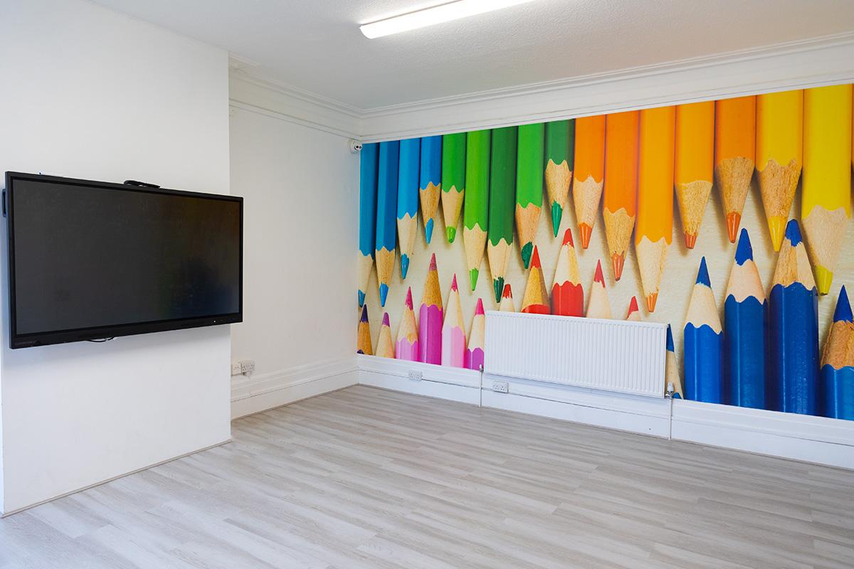A coworking classroom with a large wall-mounted screen and a colorful mural of pencil tips at The Tab HQ.