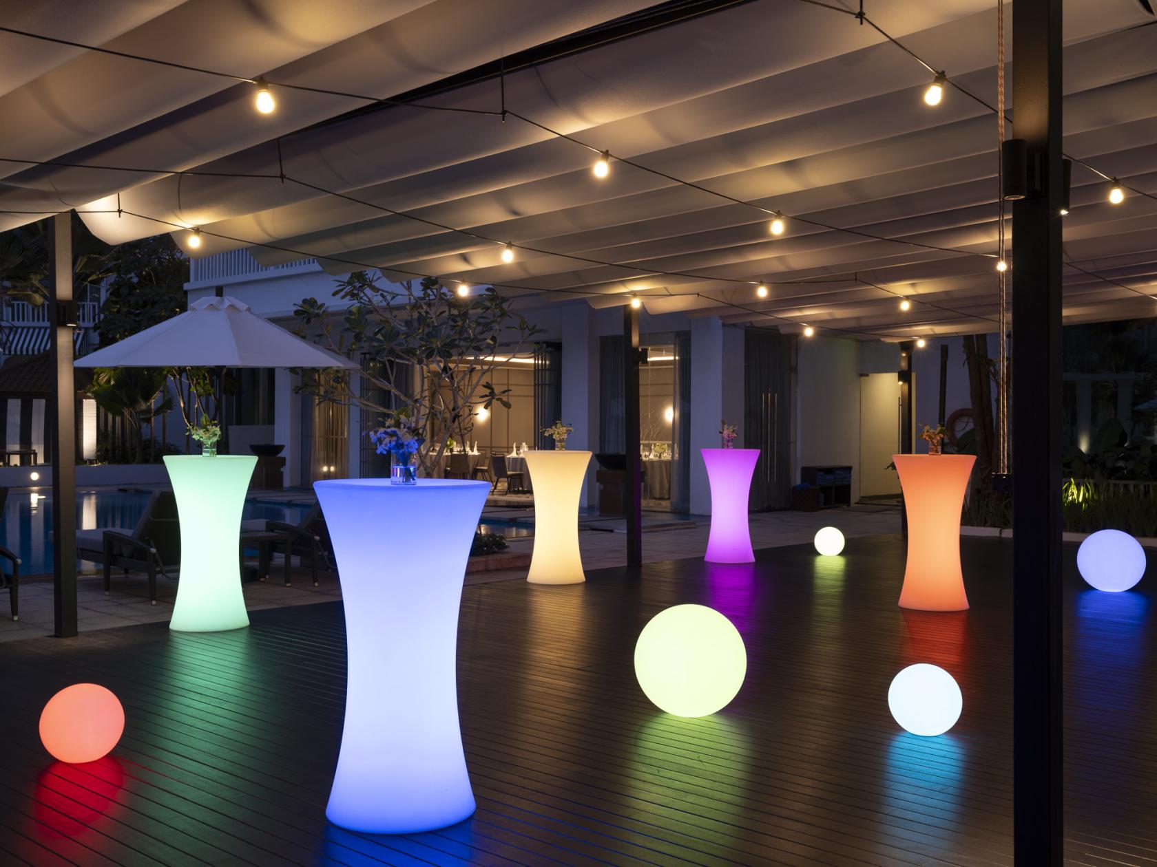 A hotel swimming pool area with glowing cocktail tables, illuminated spheres, and string lights at The Robertson House by The Crest Collection.