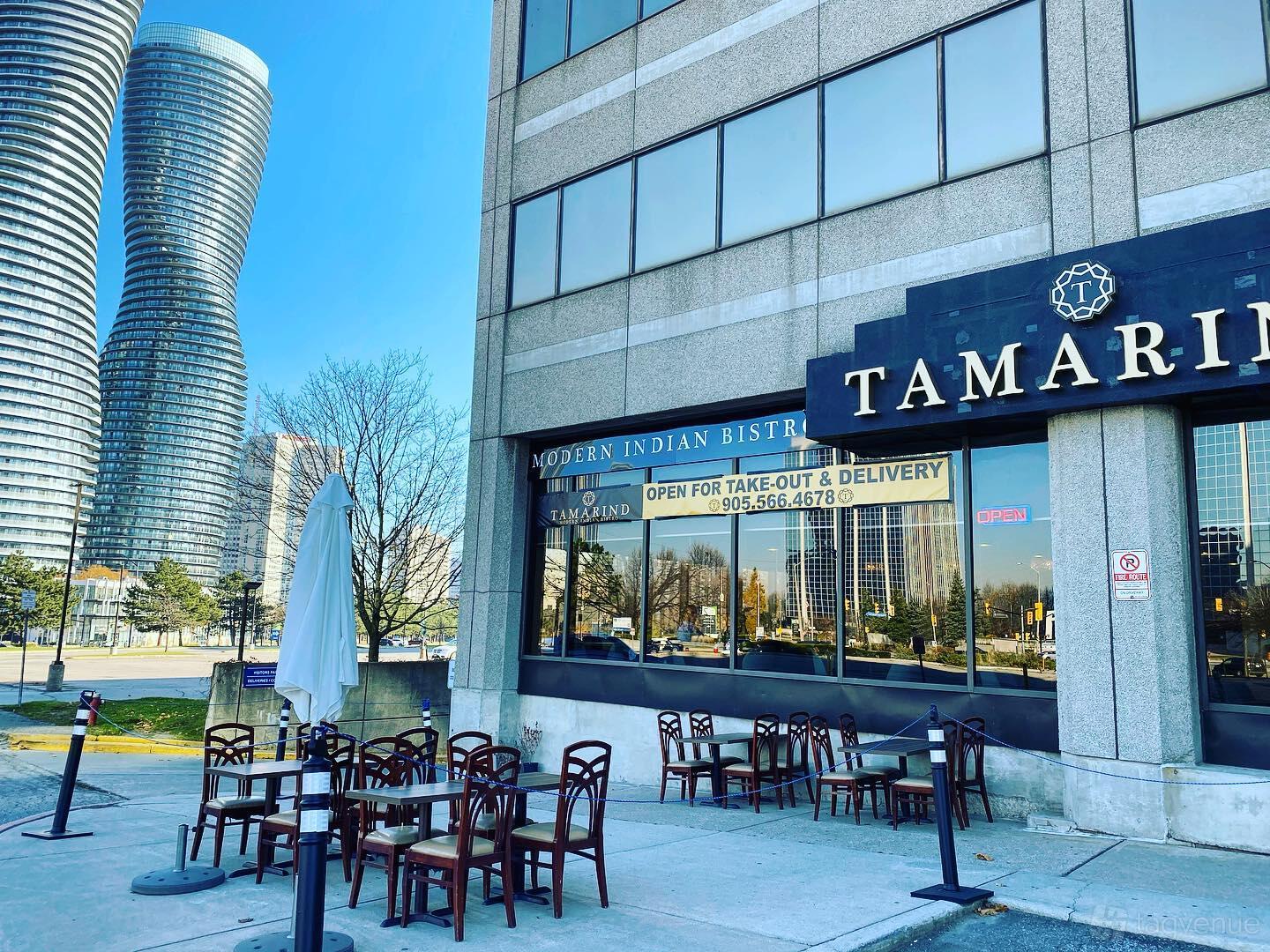A restaurant terrace with outdoor tables, chairs, and closed umbrellas along the sidewalk at Tamarind Modern Indian Bistro.