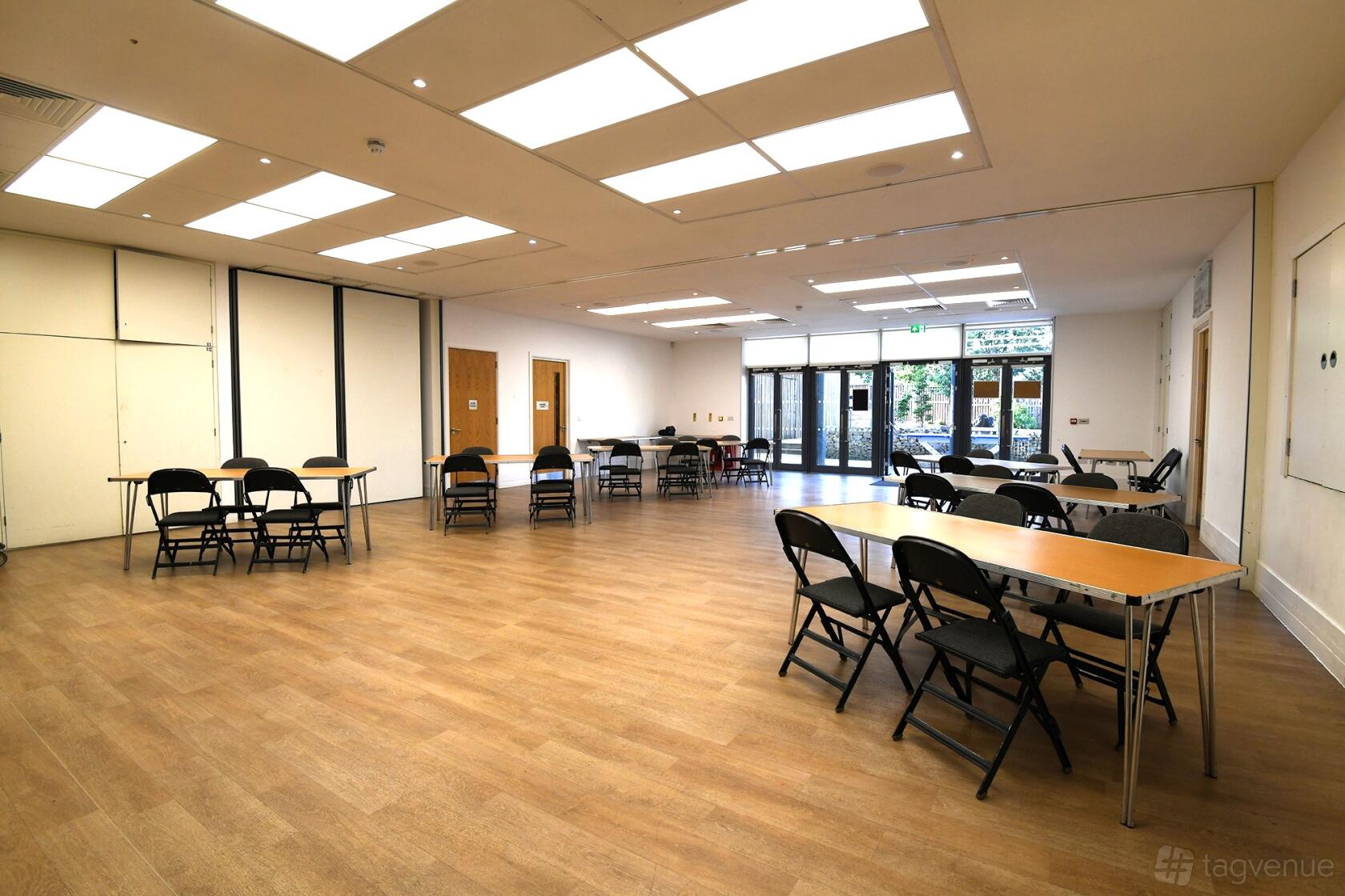 A hall with wood flooring, folding tables and chairs, and large ceiling lights at OneStonegrove.