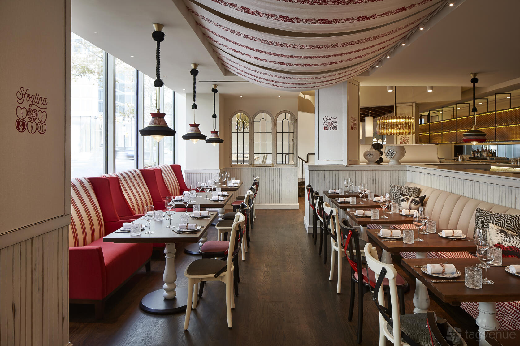 A restaurant with striped banquette seating, ceiling drapery, and floor-to-ceiling windows at Sfoglina Rosslyn.