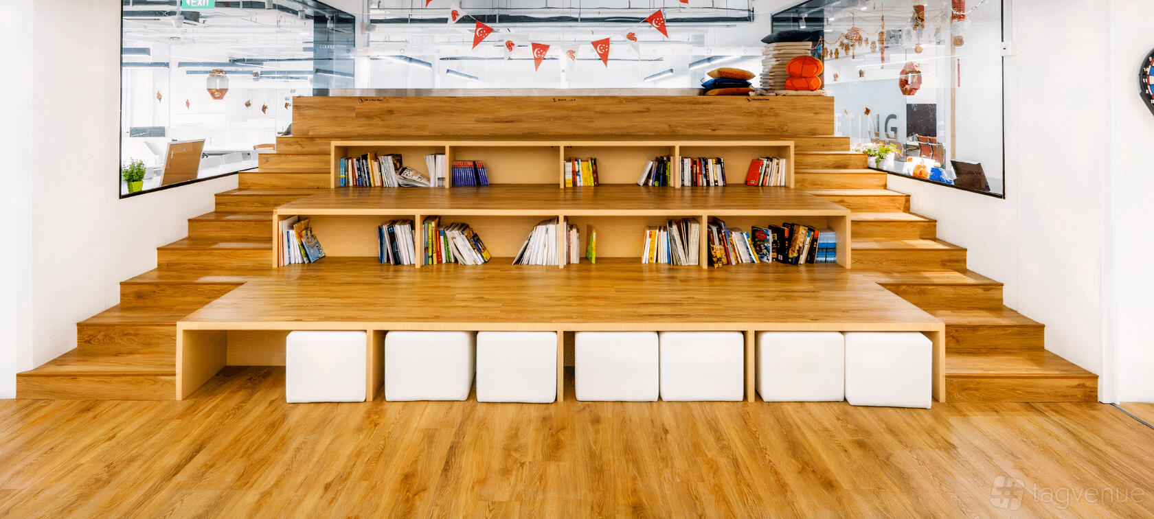 A coworking space with built-in wooden tiered seating, bookshelves, and cube seats at UClub Singapore OneNorth.