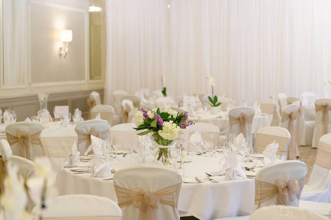 A hotel banquet hall with round tables, white linens, floral centerpieces, and draped walls at Down Hall Hotel.