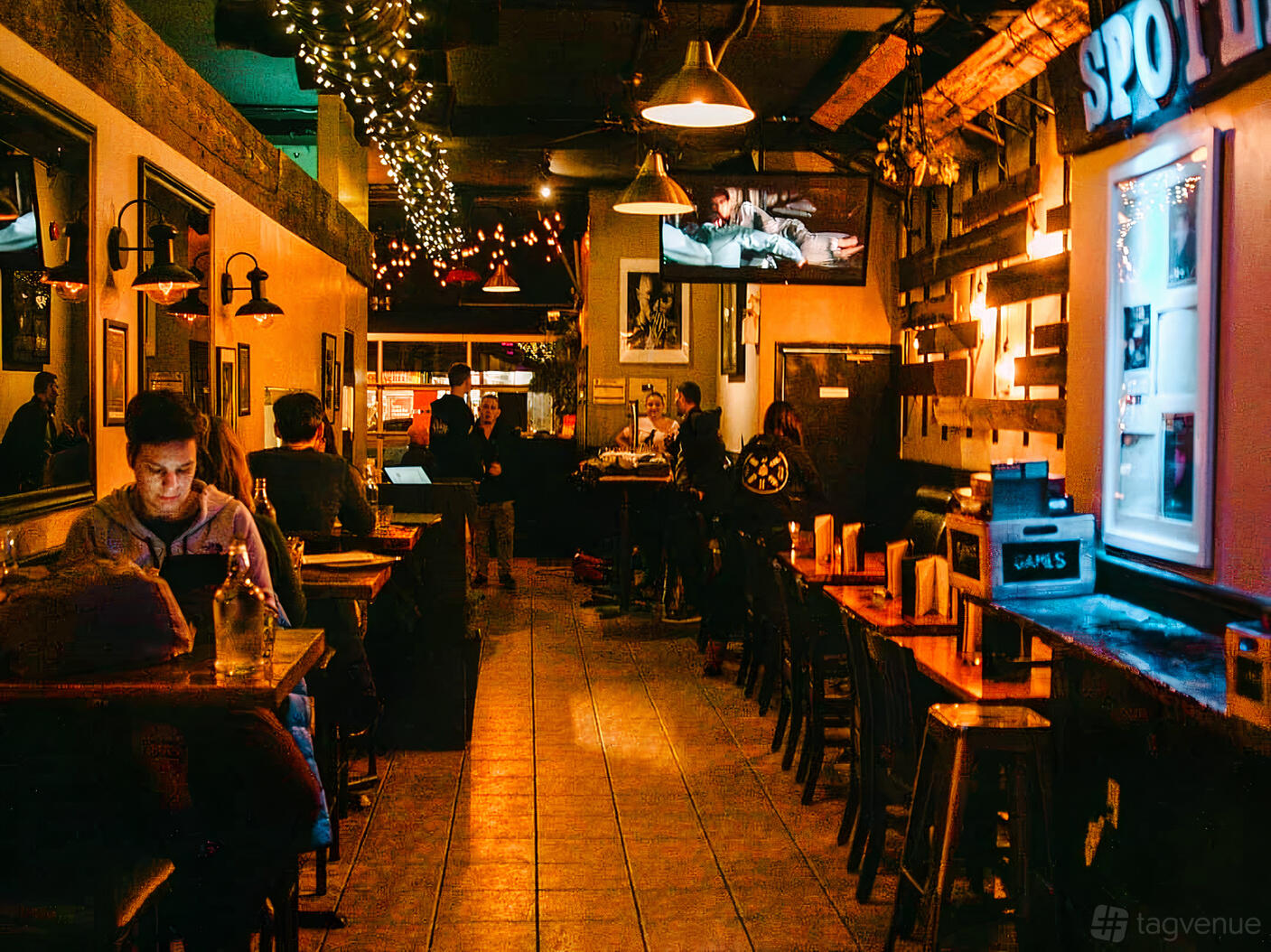 A pub bar with wooden tables, wall-mounted lights, framed pictures, and a dartboard at BAR HOP BREWCO.
