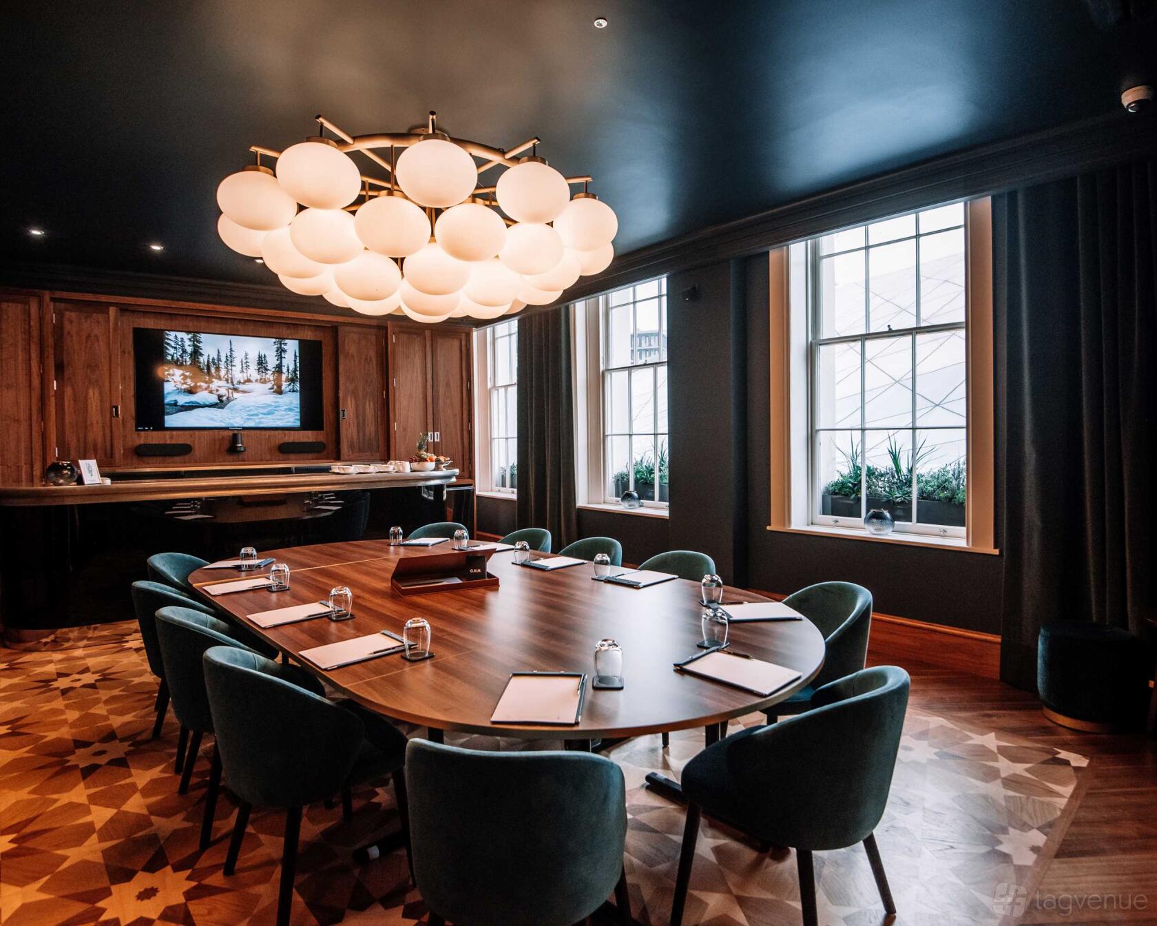 A hotel dining room with a large wooden table, velvet chairs, modern chandelier, and tall windows at Great Northern Hotel: The Carriage & Lounge.