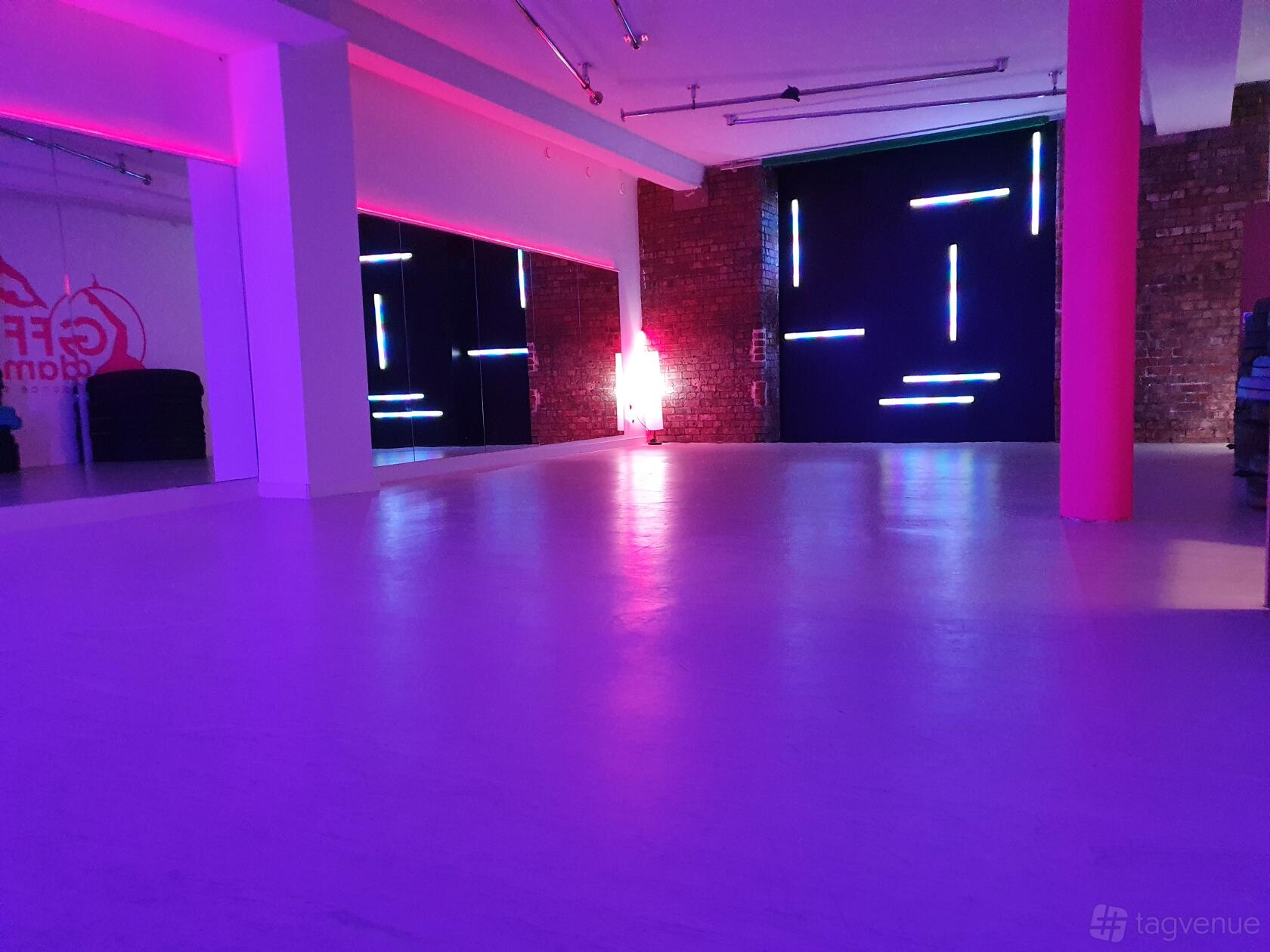 A dance studio with exposed brick walls, mirrored wall, and colored LED accent lighting at GFFdamian Dance Studio.