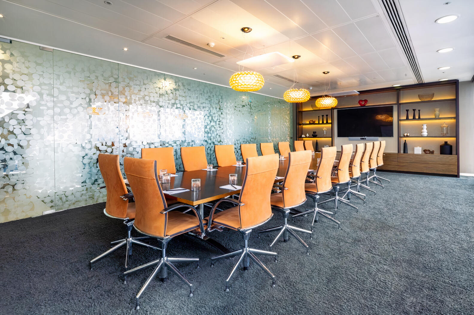 A meeting room with a long table, orange leather chairs, glass wall divider, and pendant lighting at Landmark: Heron Tower, London.