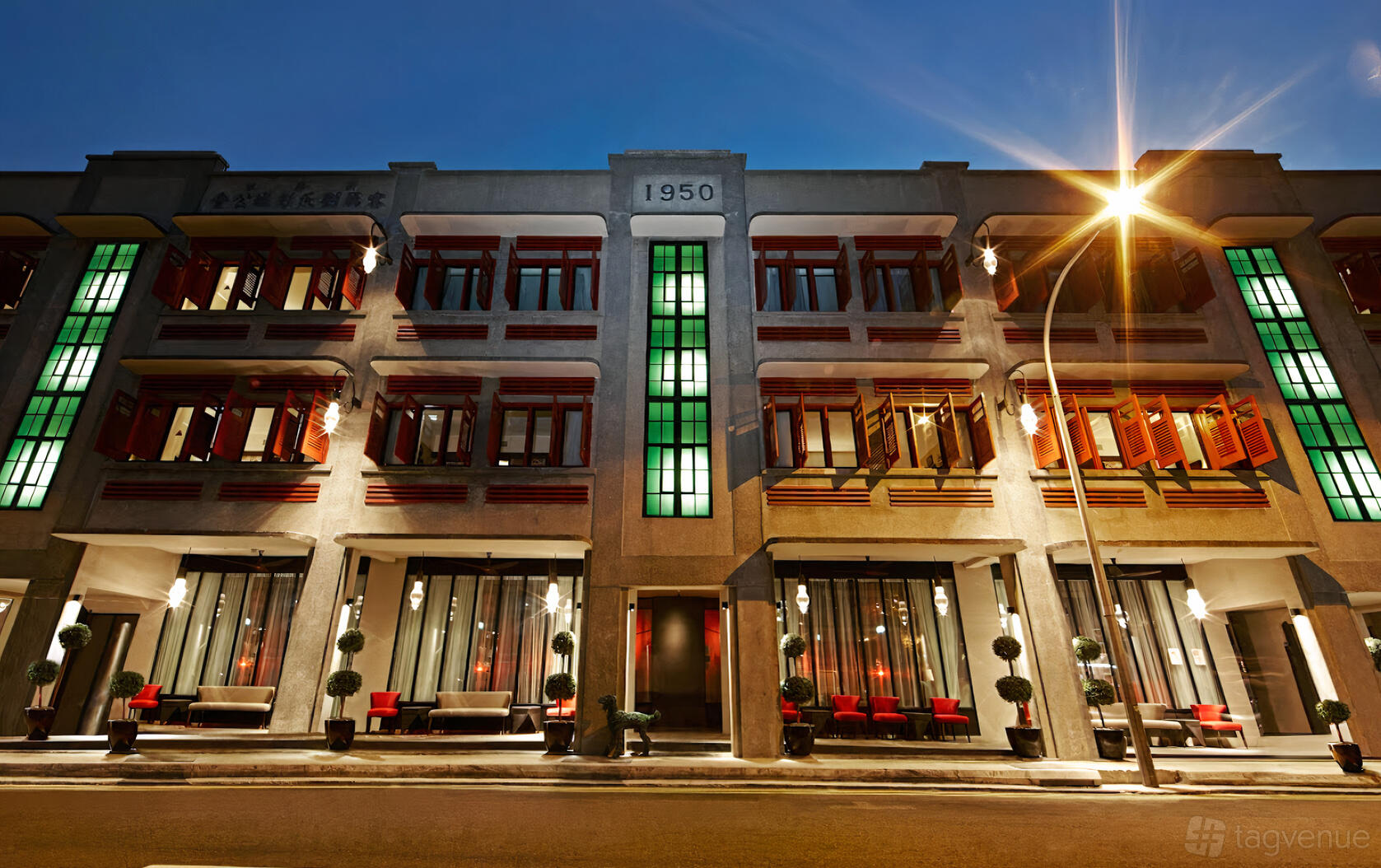 A hotel with art deco facade, red window shutters, green glass panels, and illuminated entrance at The Vagabond Club Singapore.