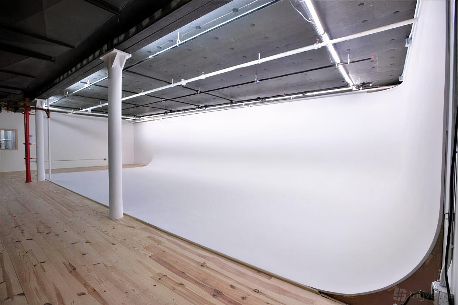 A recording studio with a large white cyclorama wall, exposed ceiling pipes, and light wood floors at MCM Stages.