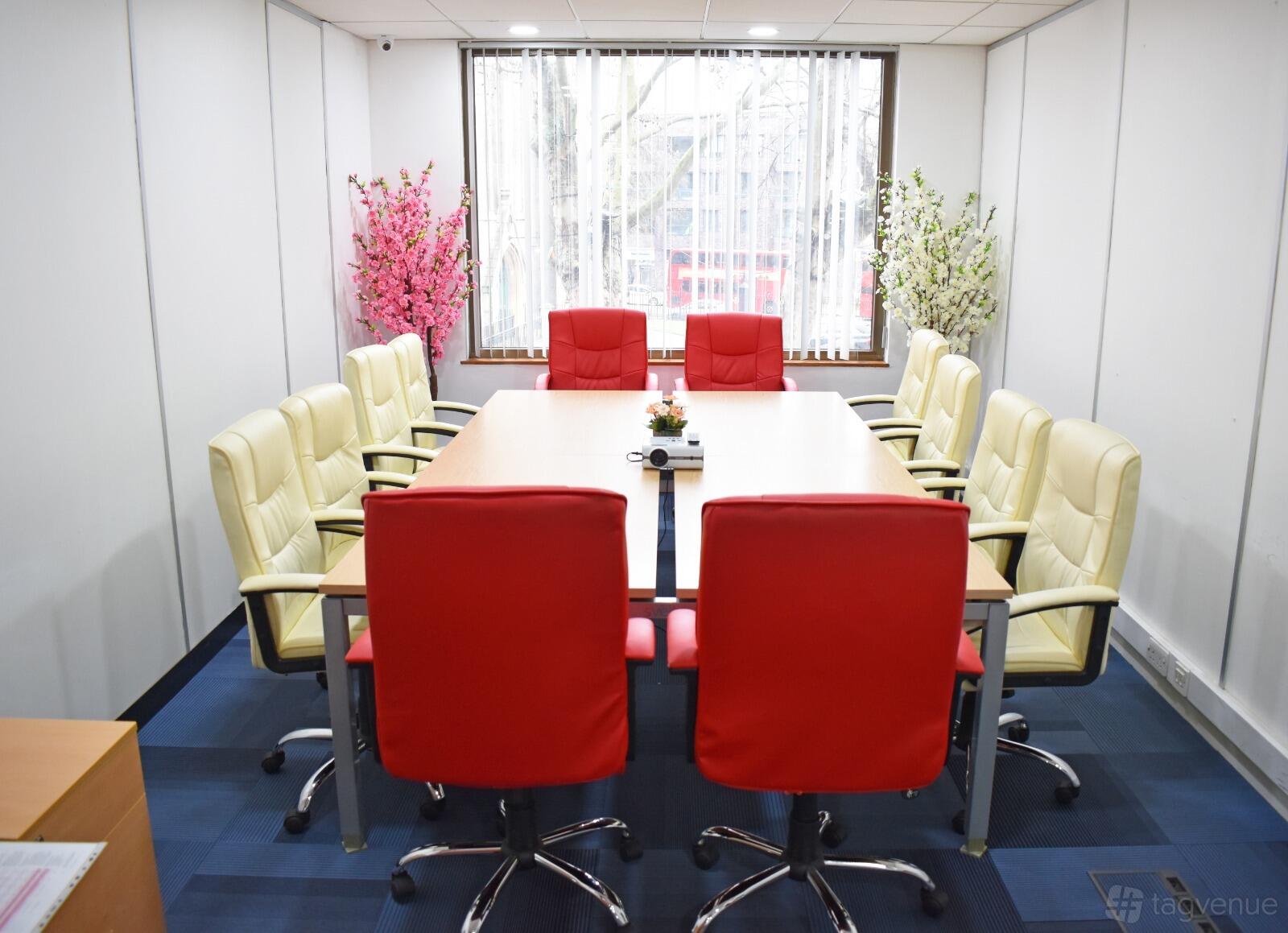 A meeting room with red and cream chairs around a rectangular table and large window at Stratford.