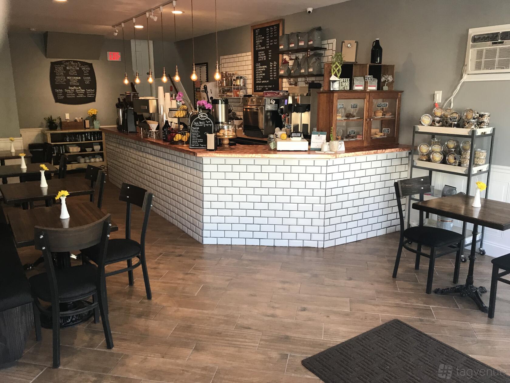 A cafe with a white subway tile counter, wooden tables with vases, and a chalkboard menu at Main Street Coffee.