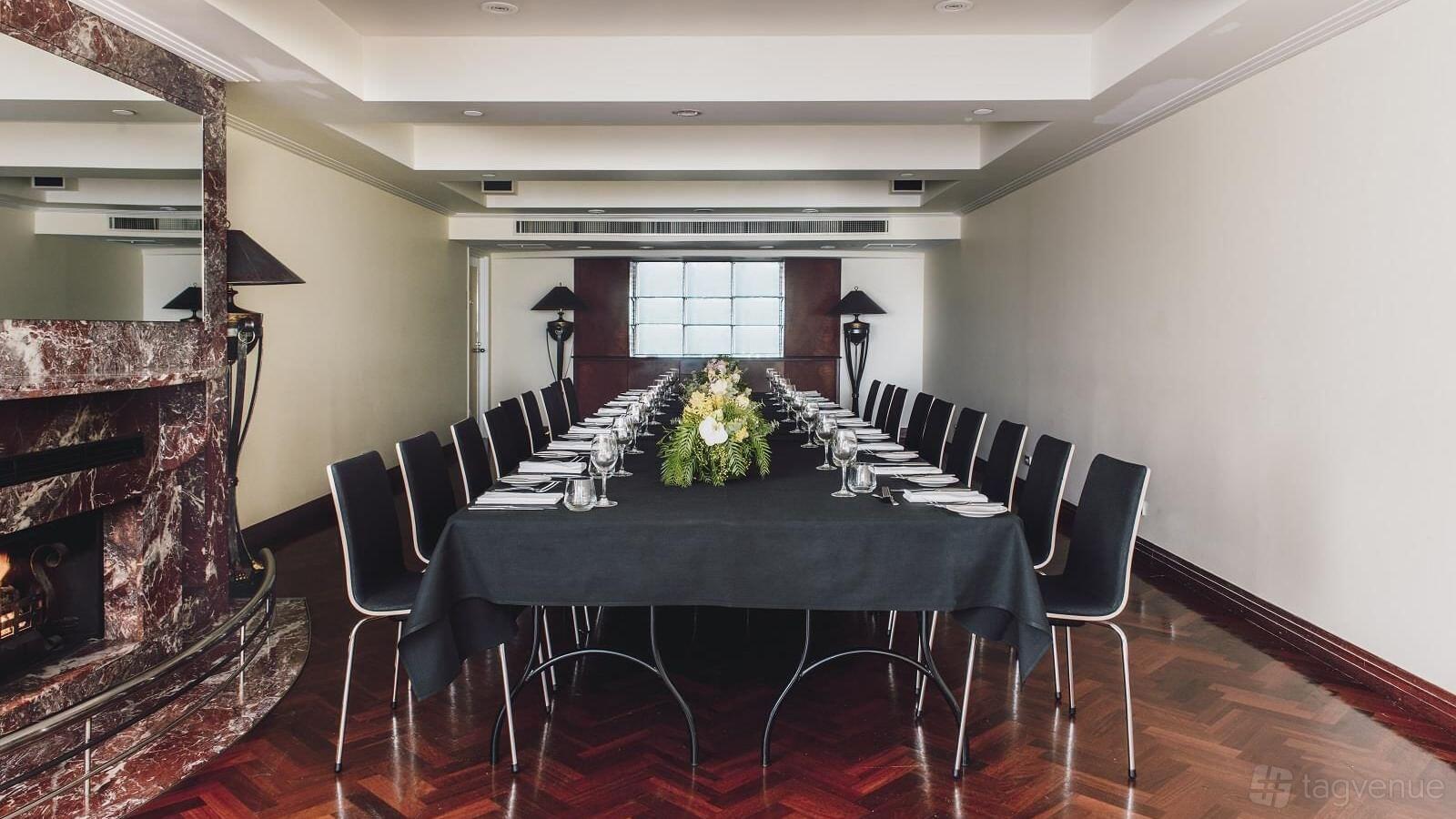 A hotel meeting room with a long U-shaped table, black chairs, and floral centerpiece at The Como Melbourne.