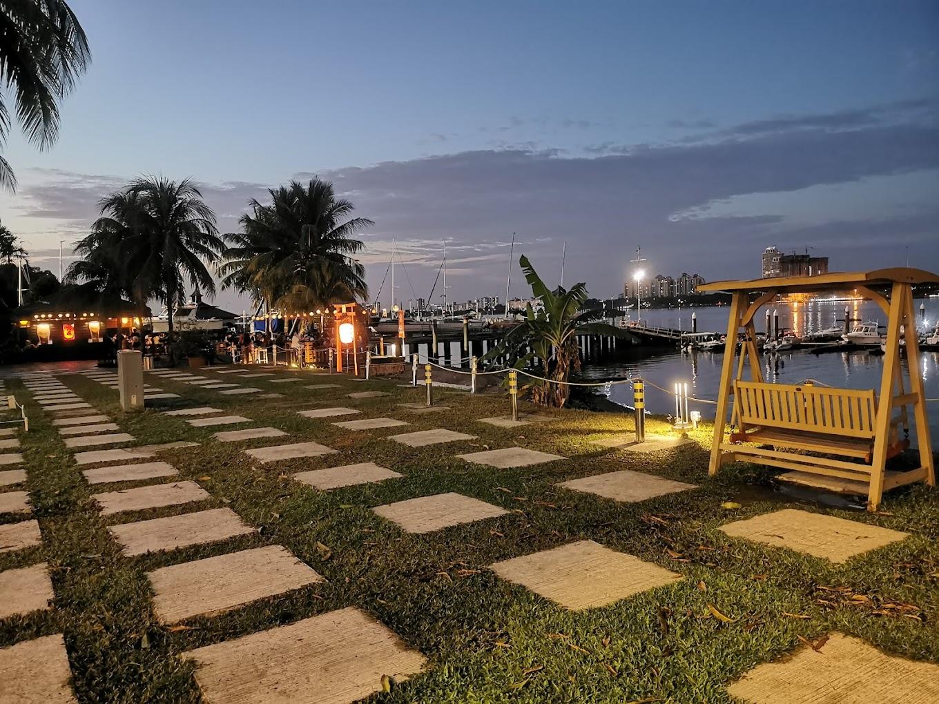 An outdoor lawn with palm trees, stone pathways, a wooden swing, and waterfront views at SAF Yacht Club.