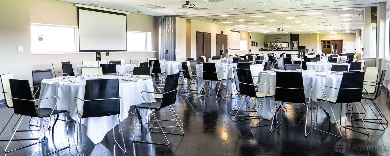 An event suite with round tables covered in white linens and black chairs at Northampton Saints Stadium.