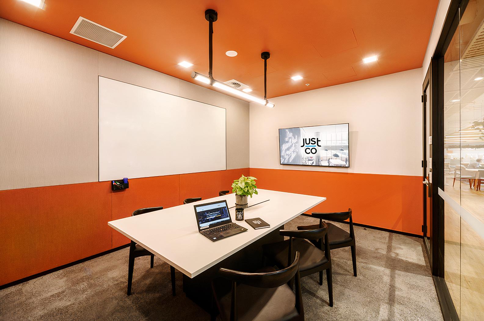 A meeting room with a rectangular table, six black chairs, wall-mounted screen, and a whiteboard at JustCo at Pitt Street.