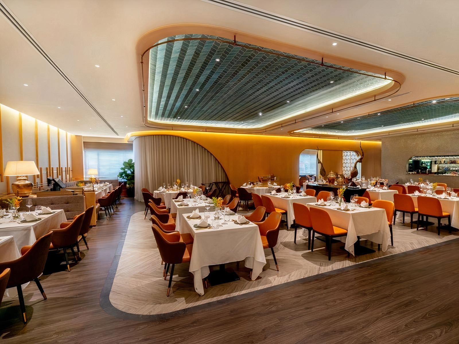 An event space in a restaurant with orange chairs, white tablecloths, and warm lighting at SARAI FINE THAI.