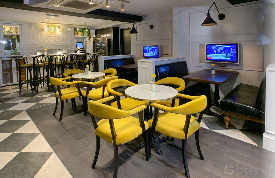 A lounge in a pub with yellow velvet chairs, marble tables, and built-in booth seating at Bonds Gin Lounge.