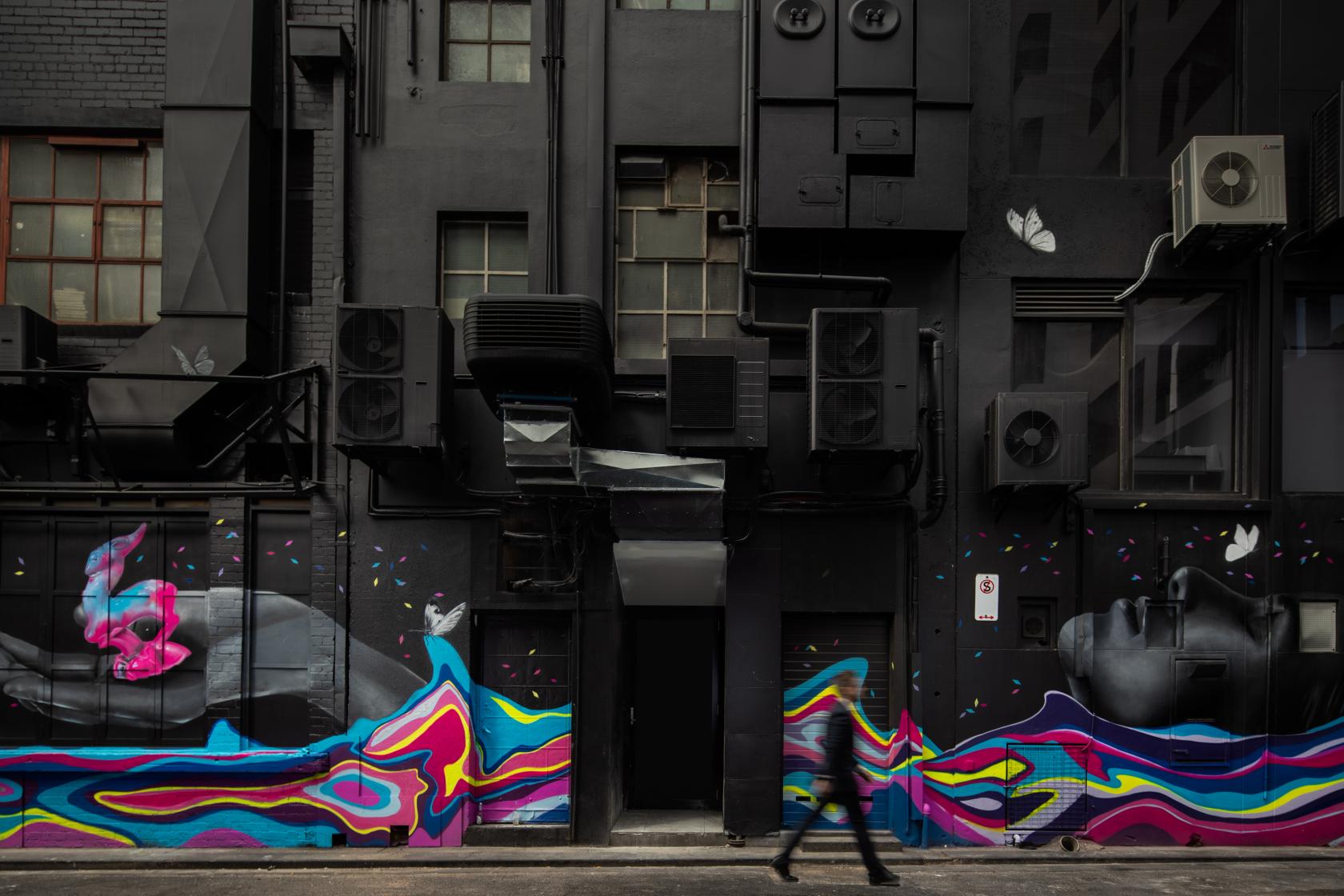 A hotel exterior with colorful street art murals, air conditioning units, and dark walls at Pullman Melbourne City Centre.