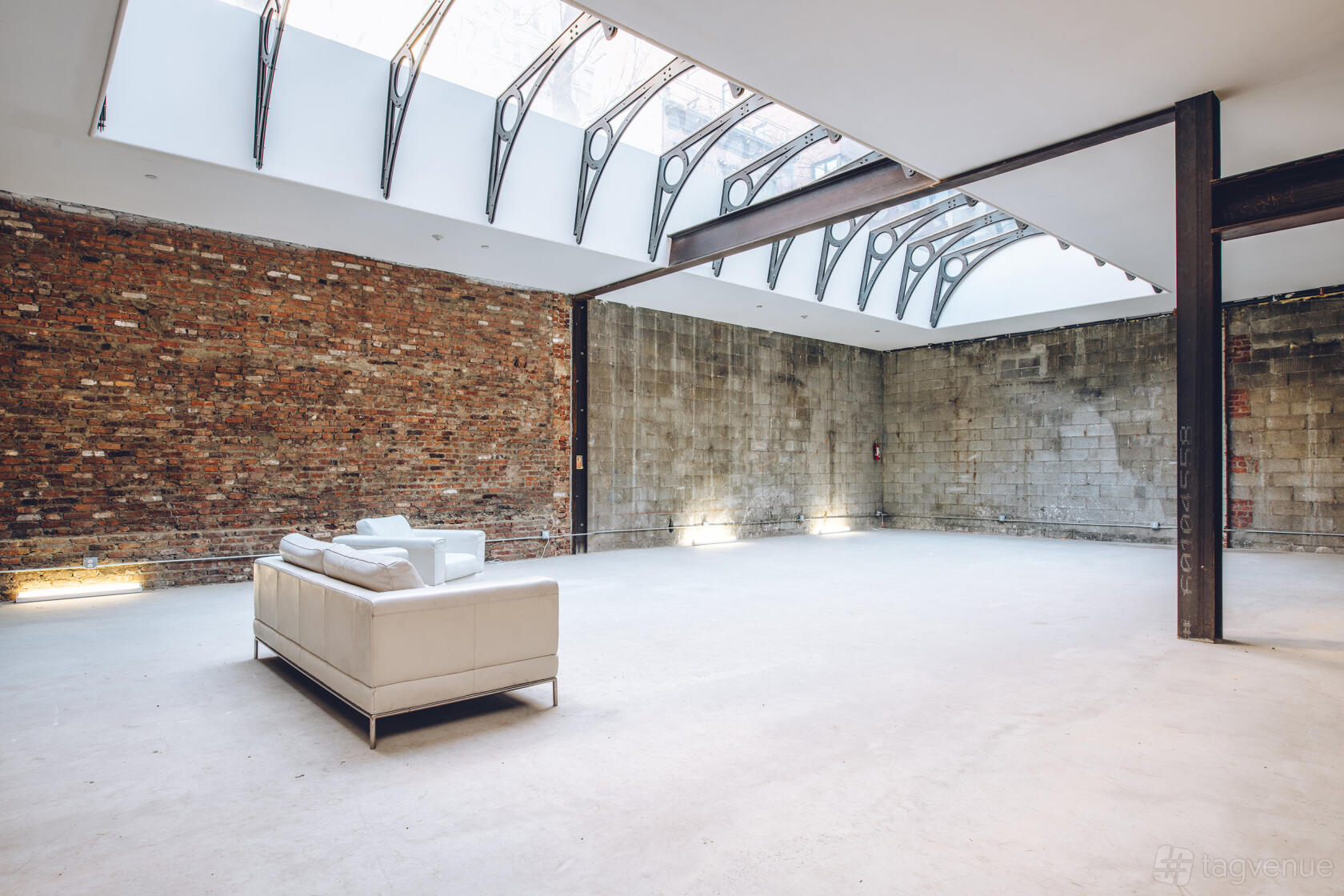 An event venue with a glass ceiling, exposed brick wall, and a white sofa at Ideal Glass Studios.