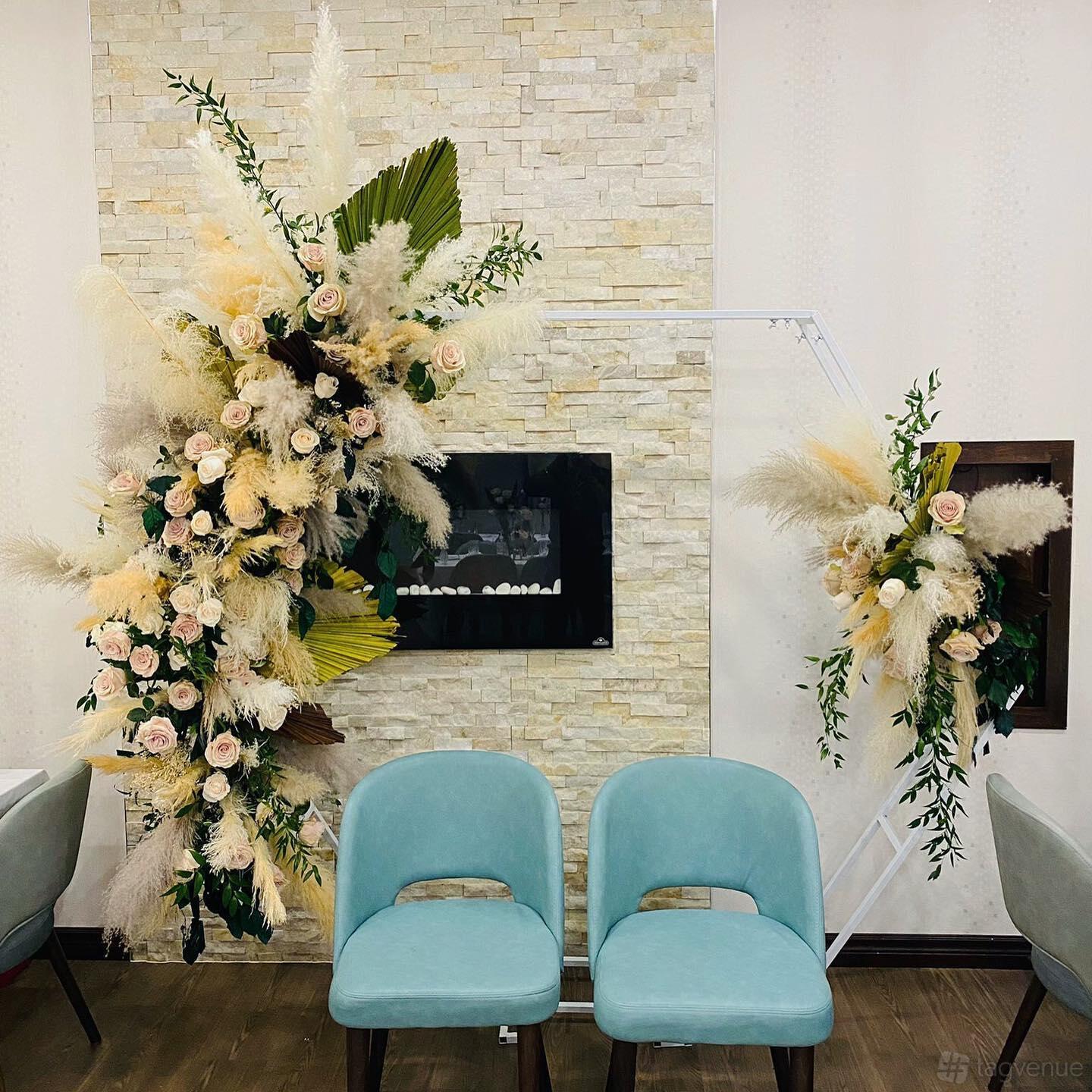 A function room with a stone accent wall, fireplace, teal chairs, and floral arrangements at Tamarind Modern Indian Bistro.