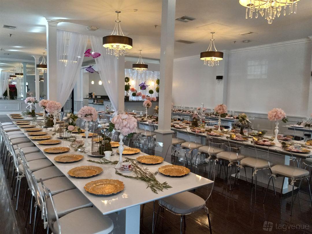 An event venue with long banquet tables featuring gold charger plates, pink floral centerpieces, and chandeliers at Beverly Banquets.