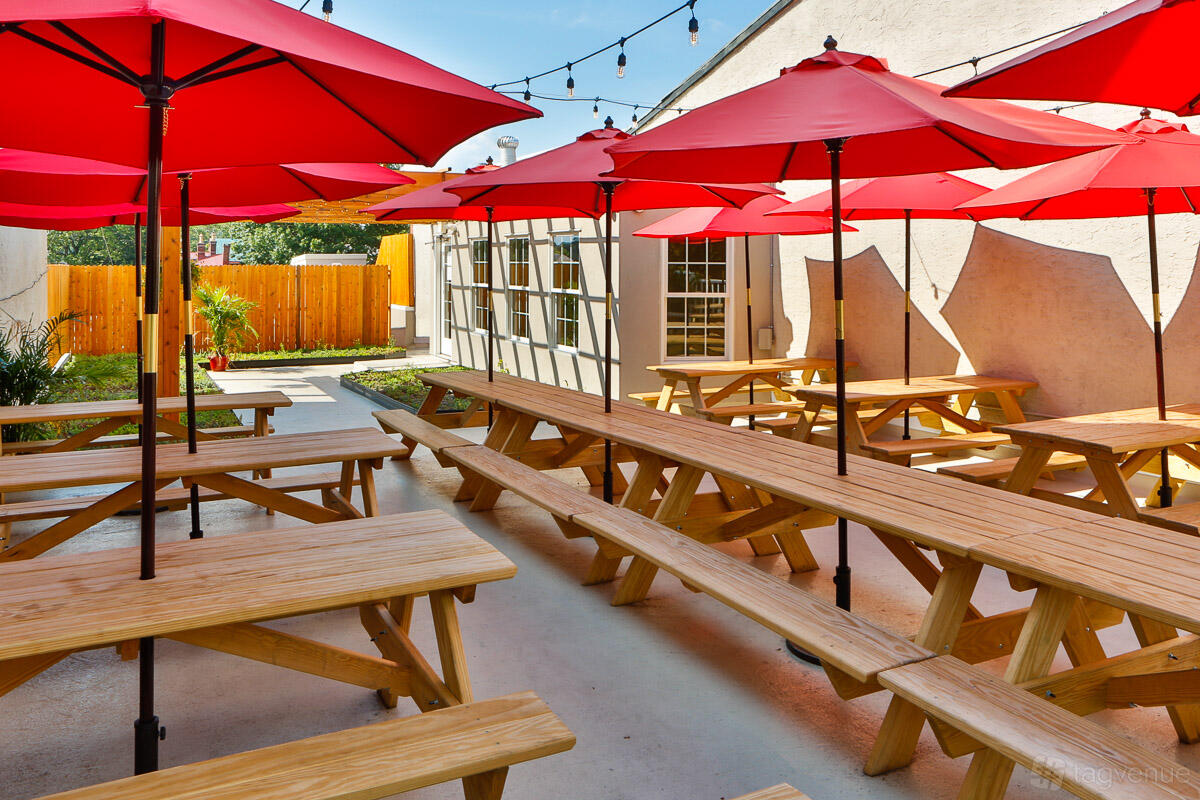A rooftop restaurant with wooden picnic tables, red umbrellas, and string lighting at The Tomato Shack Salad & Pizza co.
