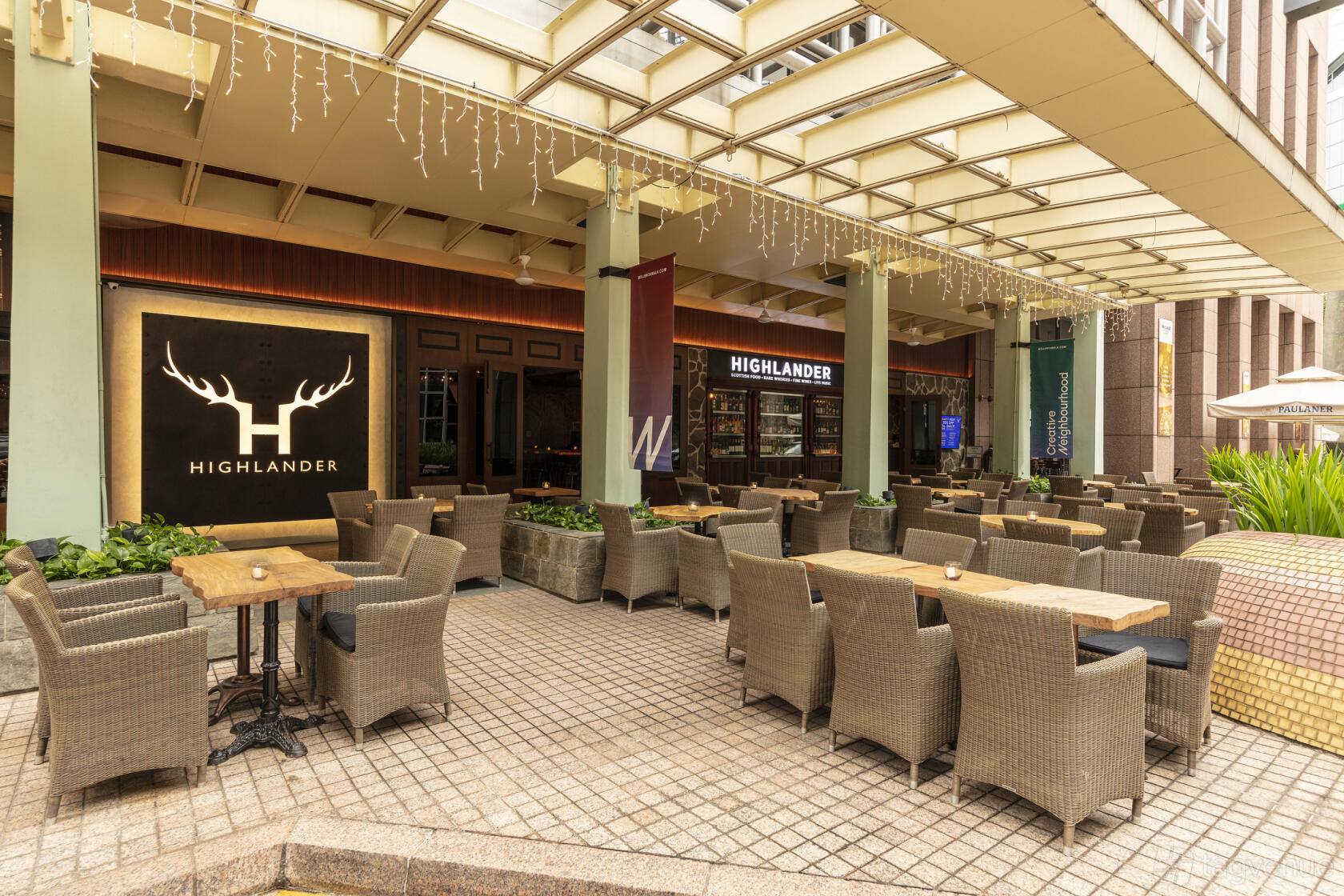 An outdoor terrace with wicker chairs, wooden tables, and string lights under a covered patio at Highlander.