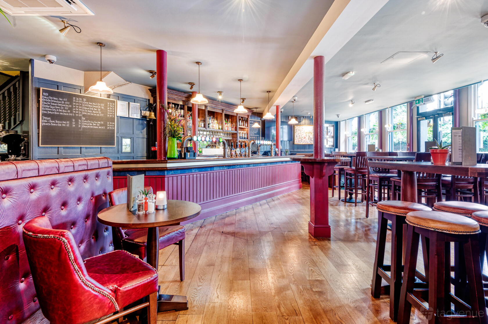 A pub with red leather banquette seating, high tables and stools, and a long wooden bar at The Volunteer, Baker Street.