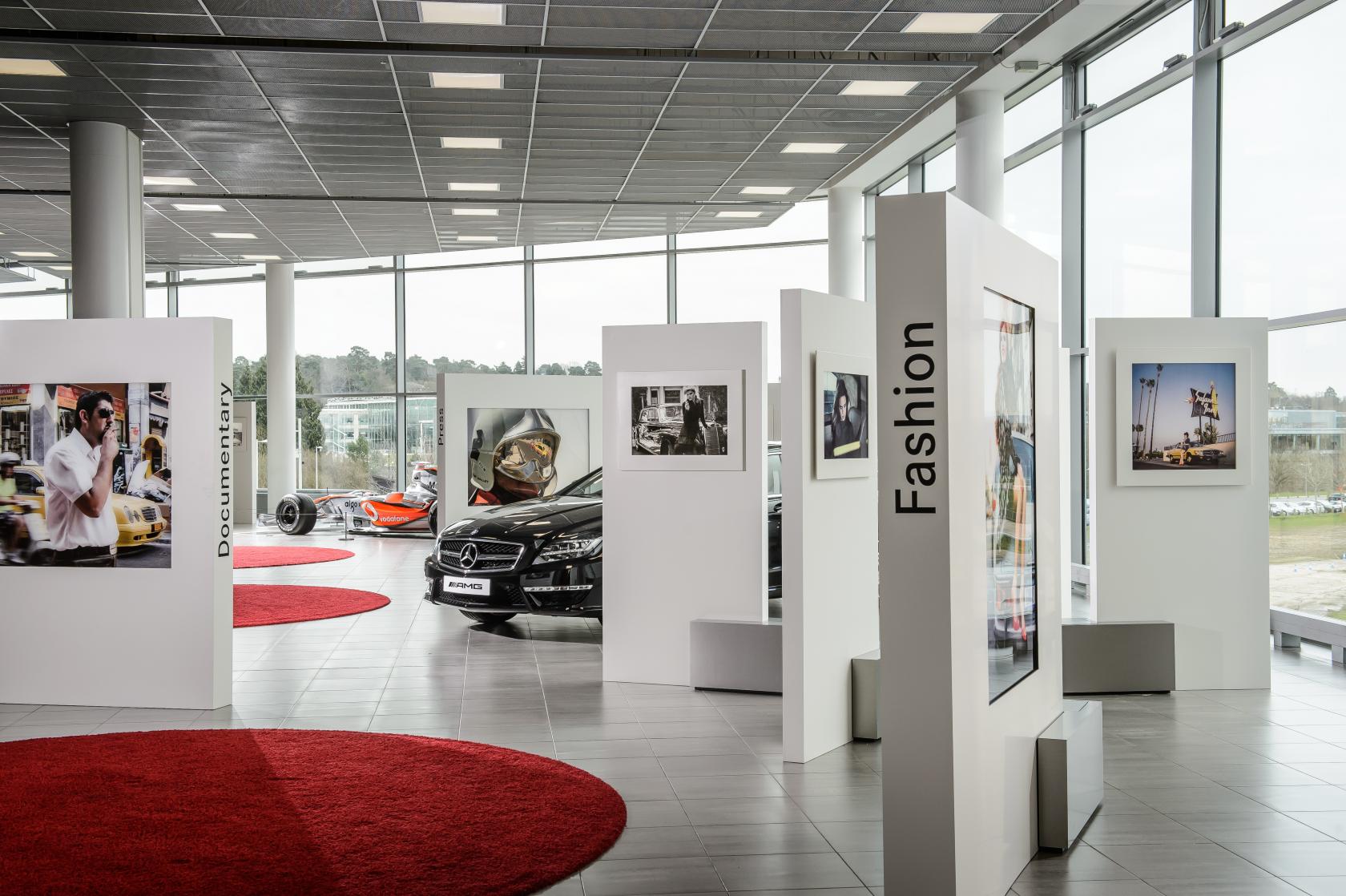 An event space with large windows, red circular carpets, car displays, and exhibition panels at Mercedes-Benz World.