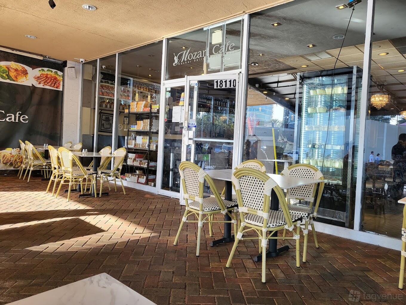 An outdoor patio with woven bistro chairs and small square tables outside glass doors at Mozart Cafe.