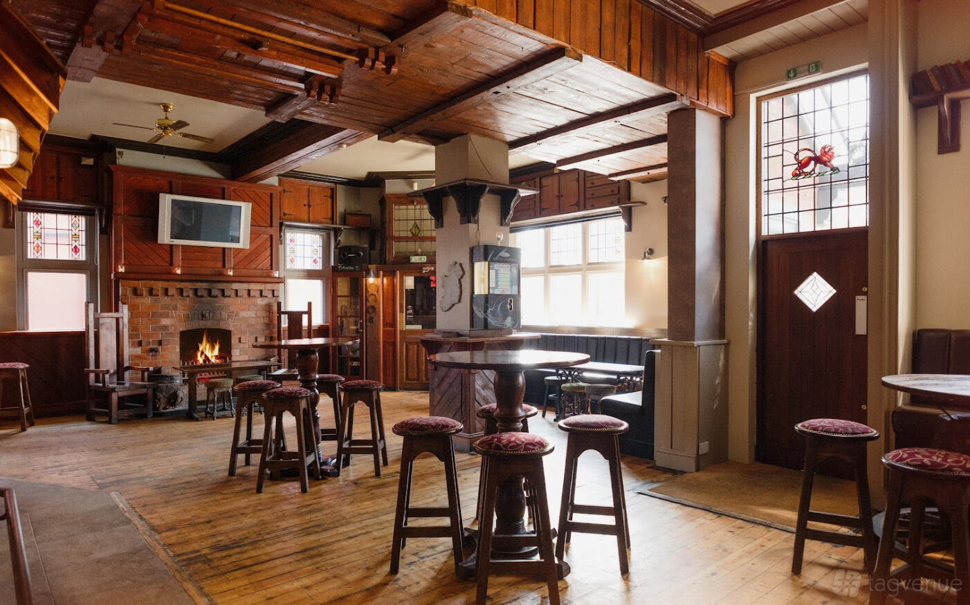 A live music venue with wooden floors, round high tables, a brick fireplace, and stained glass windows at The Castle & Falcon.