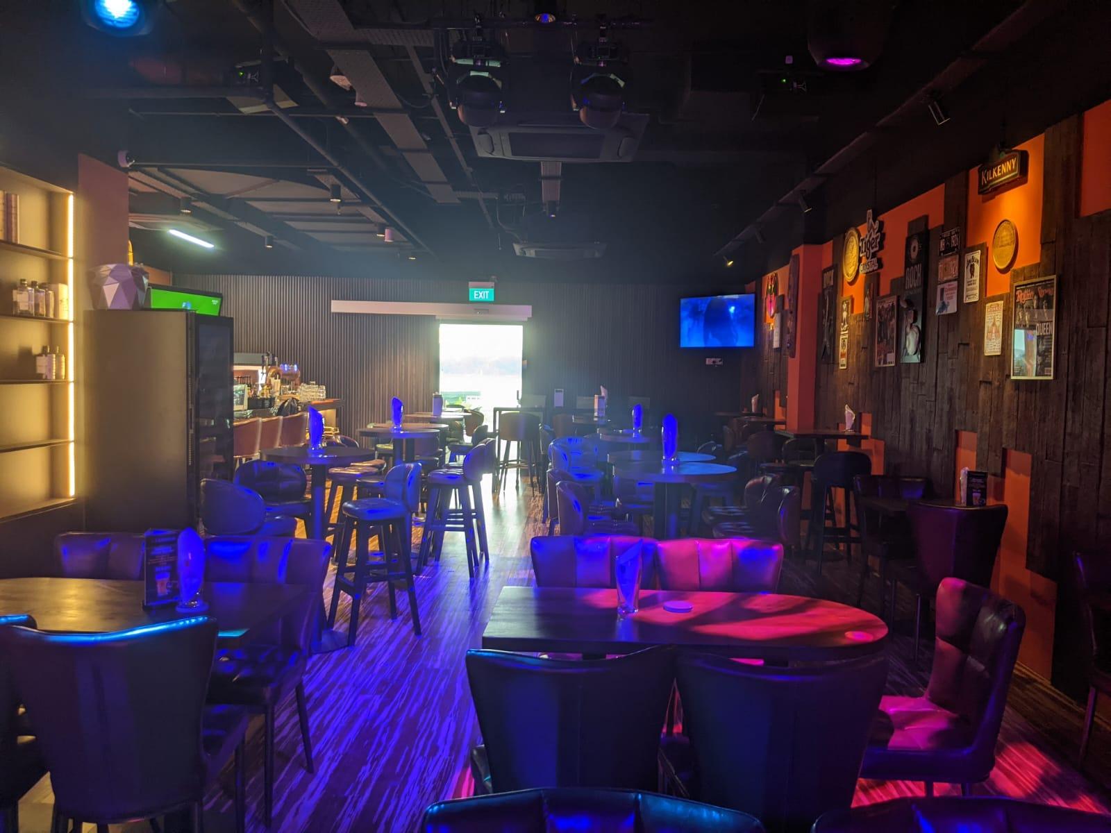 A restaurant with round wooden tables, cushioned chairs, wall art, and colorful lighting at Georges @ Waterfront (Bedok).
