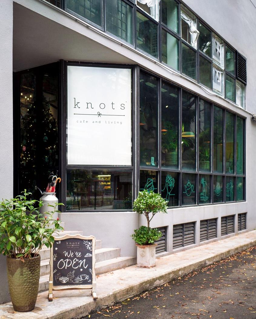 A restaurant exterior with large windows, potted plants, and cafe signage at Knots Cafe and Living (Pasir Panjang).