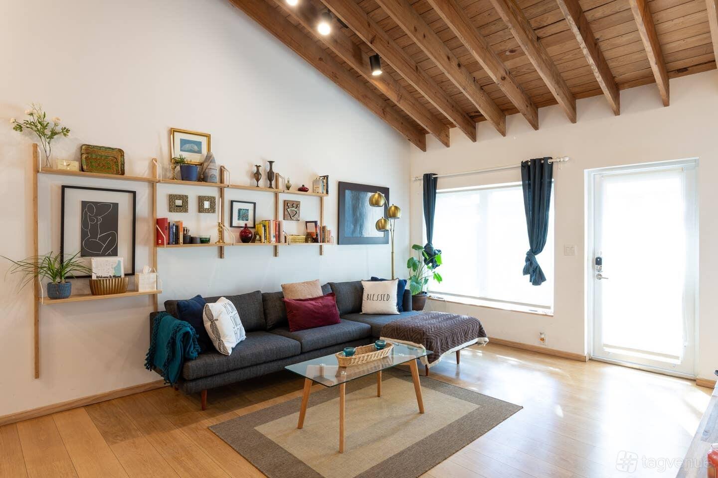 A country house living area with exposed wooden beams, a gallery wall, large windows, and a mid-century sofa at Z studio NE 68th St.