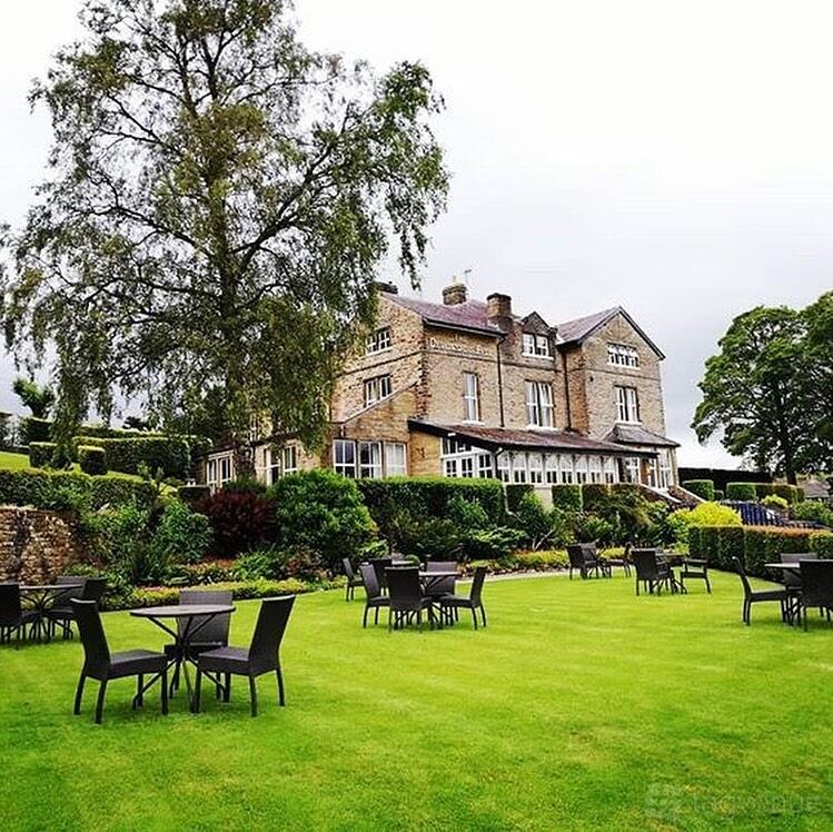 A hotel with outdoor seating on manicured lawns surrounded by hedges and trees at The Devonshire Fell Hotel & Restaurant.
