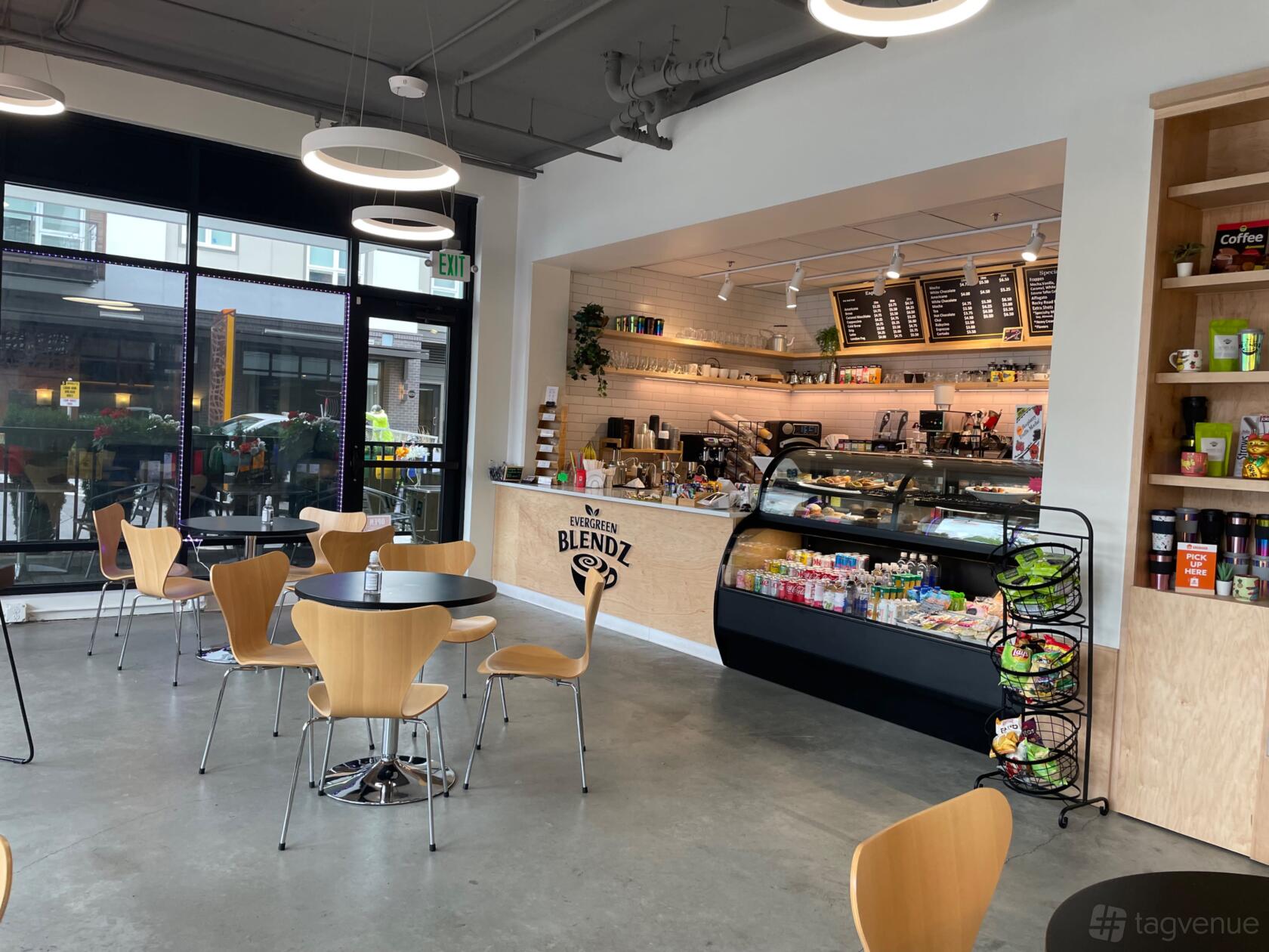 A cafe with wooden tables and chairs, a display counter with pastries, and large windows at Evergreen Blendz Coffee.