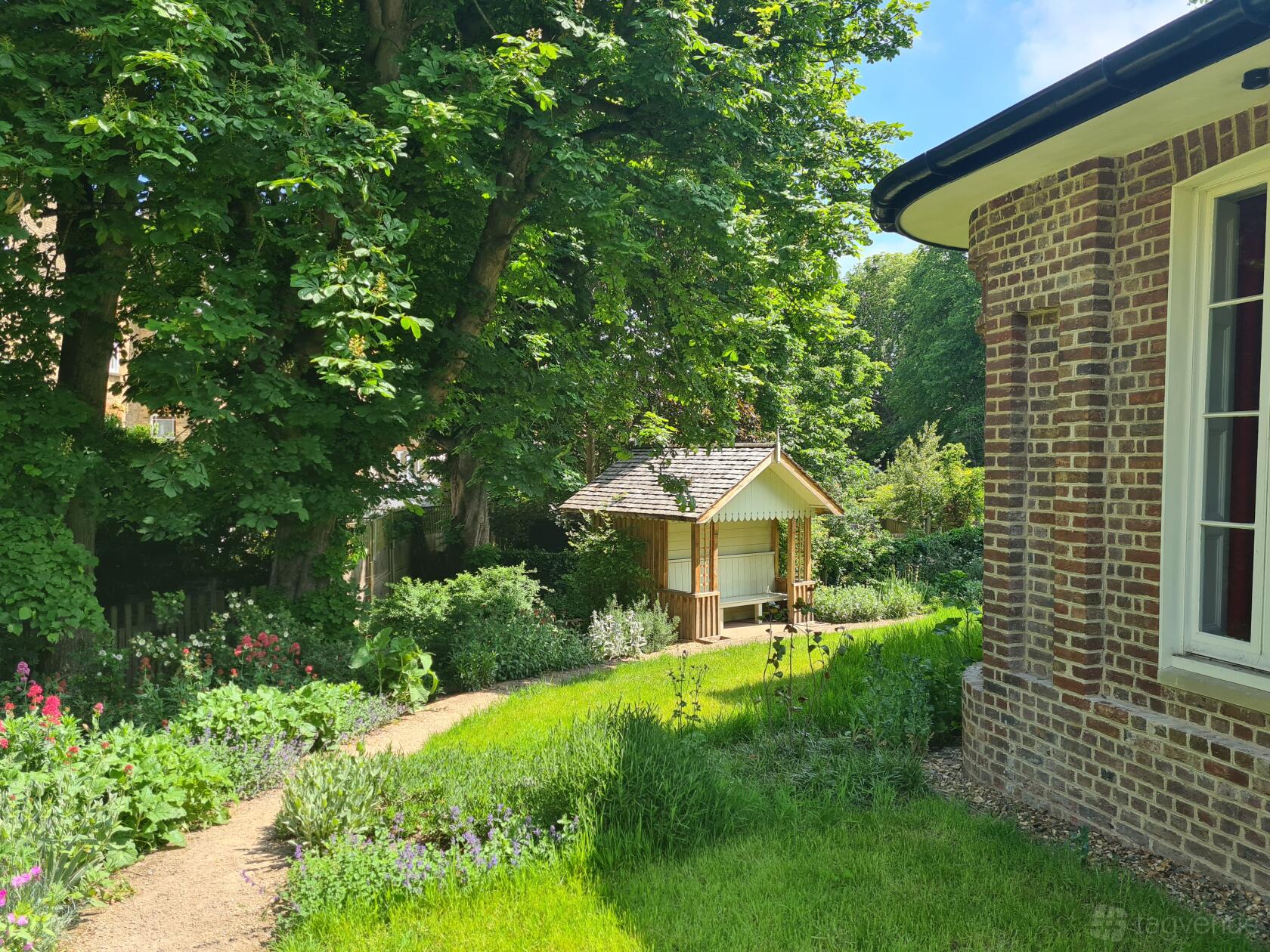 A museum garden with lush greenery, mature trees, a brick building, and a small wooden pavilion at Turner's House.