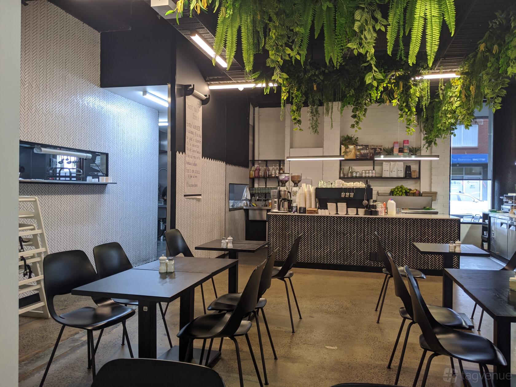 A cafe with hanging greenery, black chairs and tables, and a counter with coffee equipment at The Spade Melbourne.