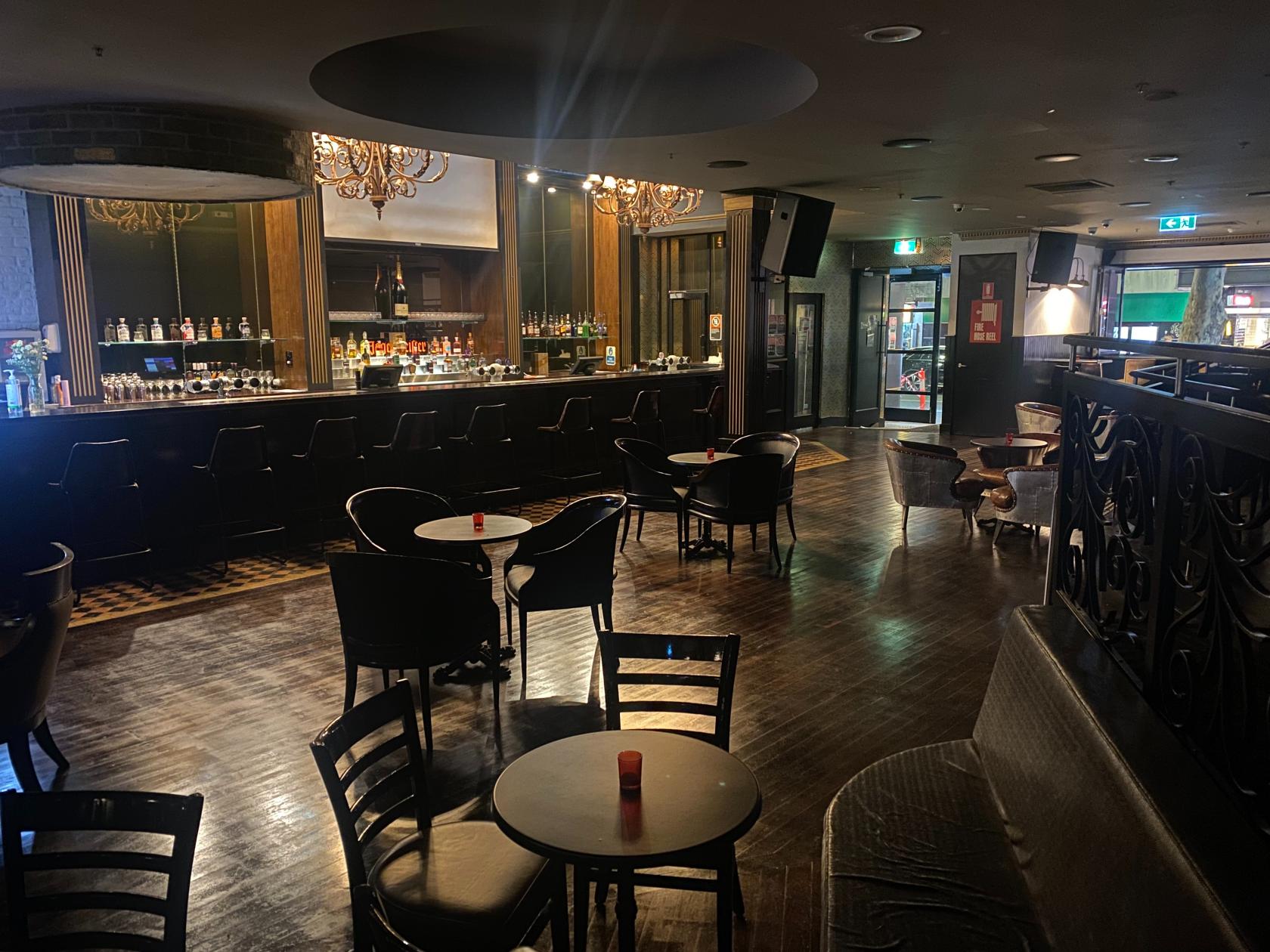 A hotel nightclub with a long mirrored bar, dark wood flooring, and round tables with candles at Sydney Elements.