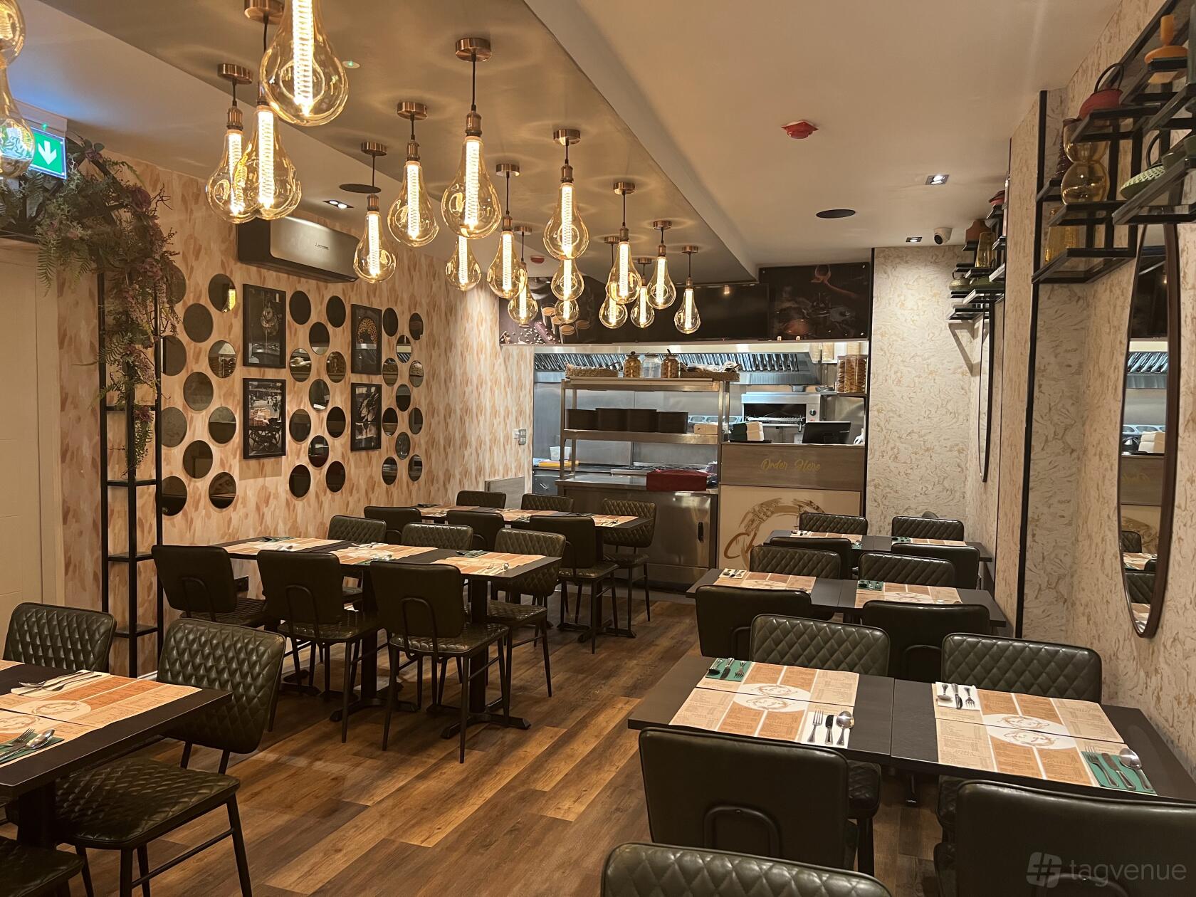 A cafe with exposed filament pendant lights, wall art, and tables set with placemats at Chai Galli.