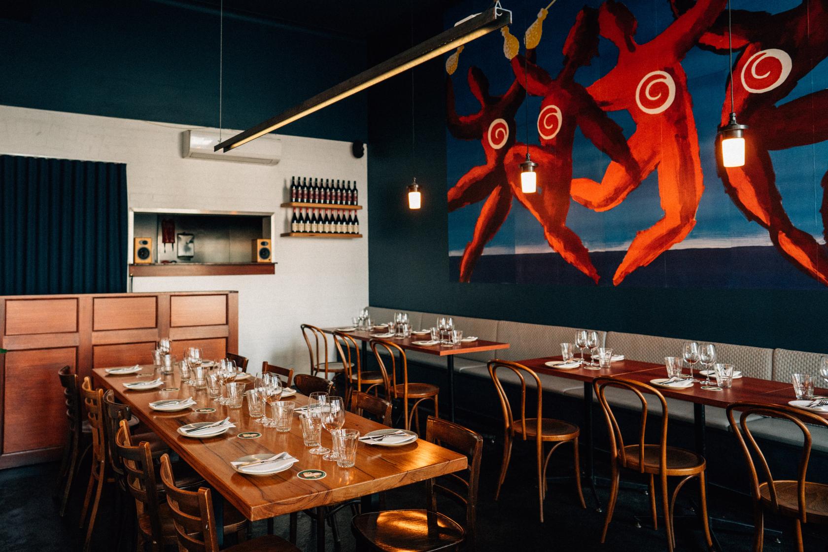 A dining room in a pub with long wooden tables, bentwood chairs, and a bold mural on the wall at The Lincoln.