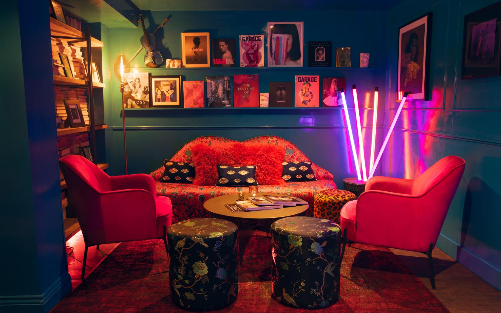 A dining room in a cocktail bar with velvet armchairs, a patterned sofa, colorful neon lights, and wall-mounted records at The Little Orange Door.