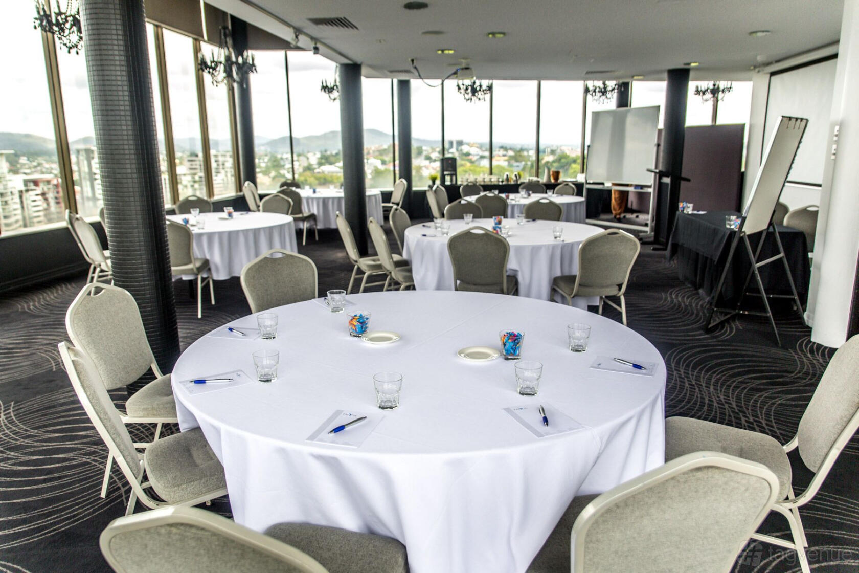 A function room with round tables draped in white linens, grey chairs, and floor-to-ceiling windows at Mercure Brisbane Spring Hill.